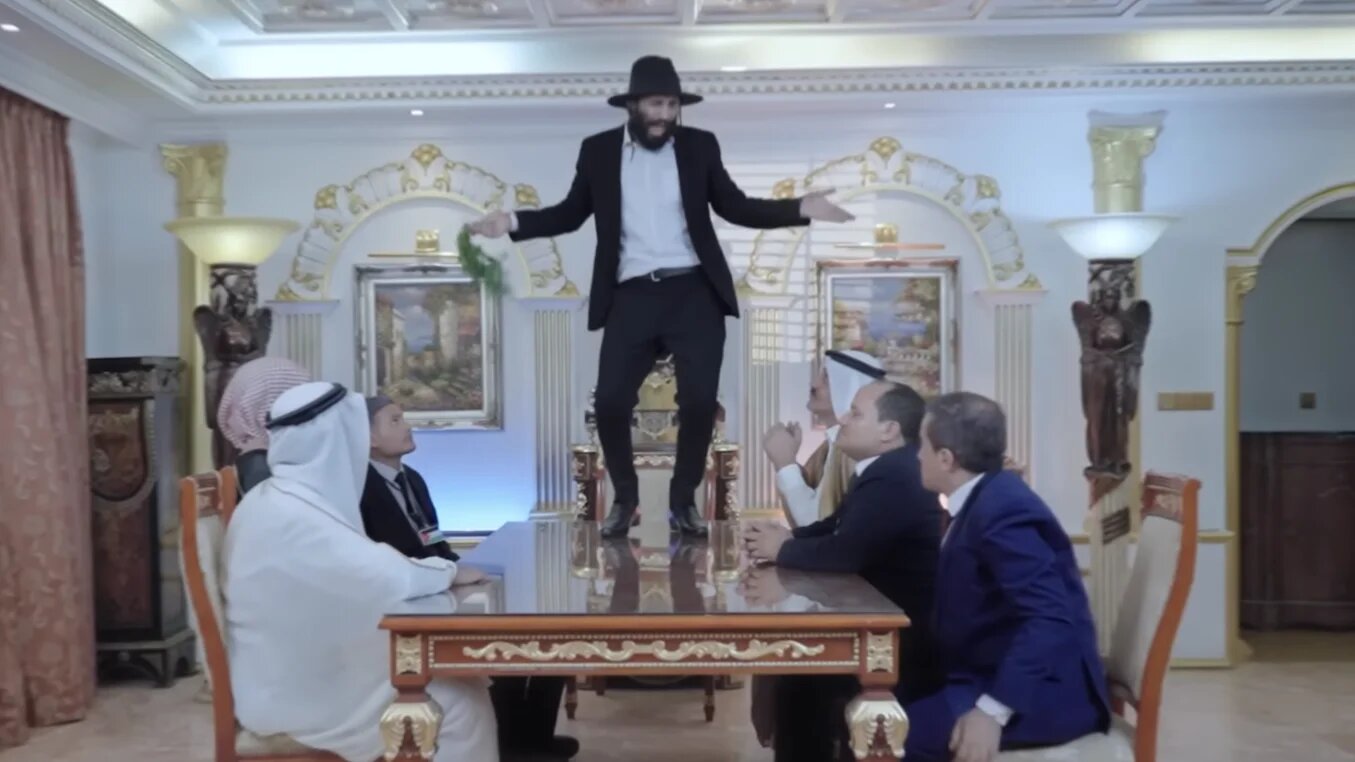 Alors que Mustafa al-Momri danse sur la table, les dirigeants arabes humiliés le regardent en souriant et l’applaudissent (capture d’écran)