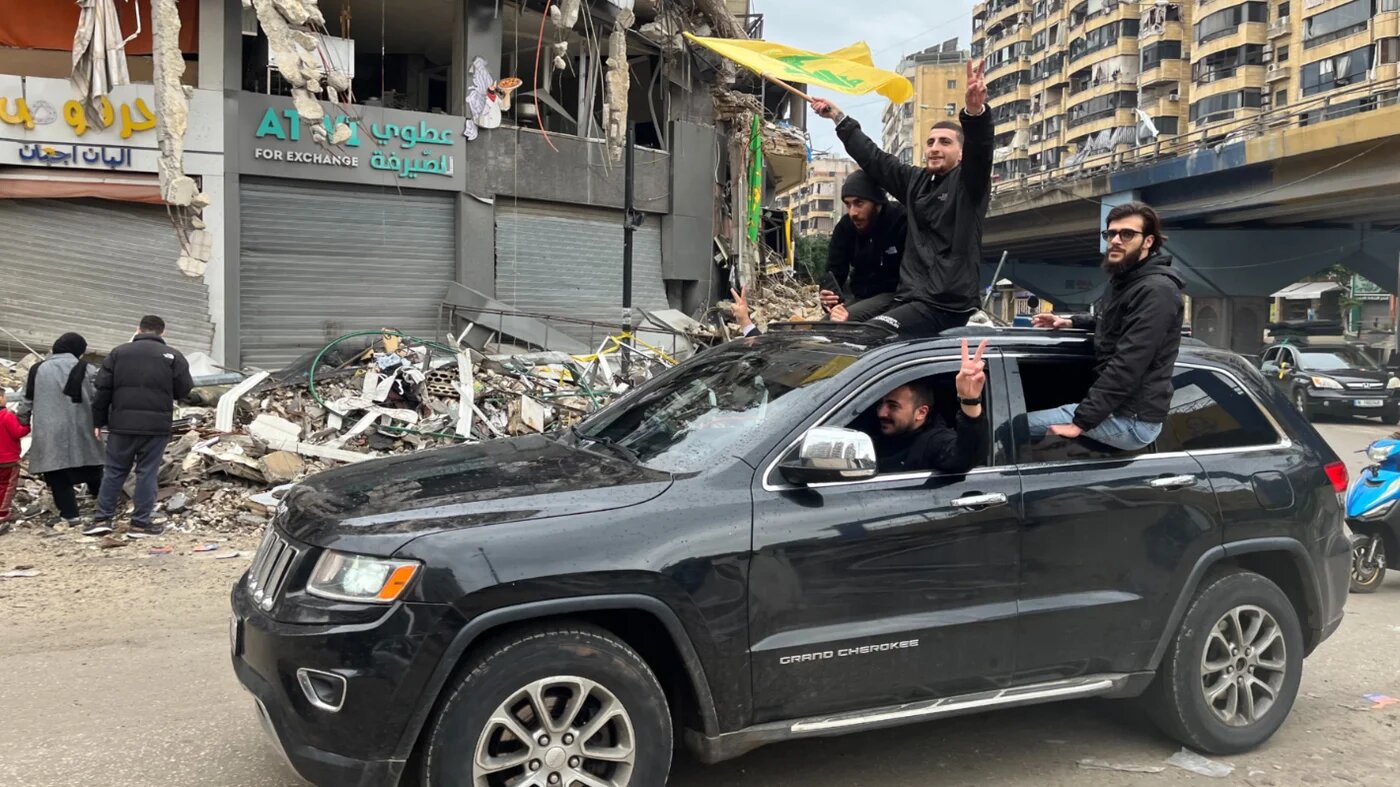 Young men wave Hezbollah flags through Dahiyeh's damaged areas in celebration of the ceasefire between Israel and Hezbollah on 27 November 2024 (Nader Durgham/MEE)