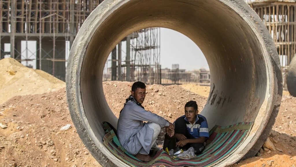 Labourers have a meal inside a concrete tube at a construction site at Egypt's New Administrative Capital megaproject, some 45 kilometres east of Cairo, on 3 August 2021 (AFP)