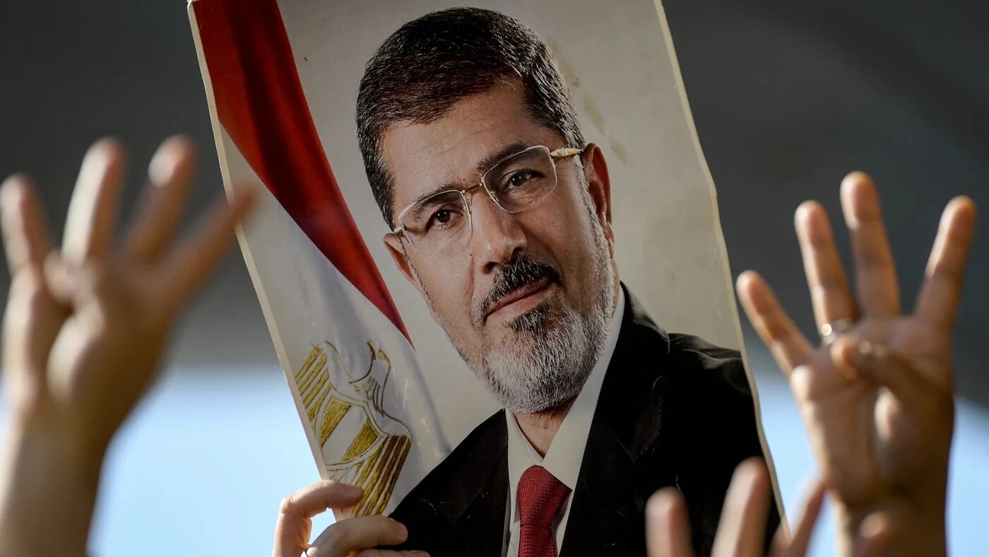 In this file photo, people flash the Rabaa sign (four-fingered hand sign by anti-coup activists ), next to a poster of late Egyptian President Mohamed Morsi during a symbolic funeral ceremony on 18 June 2019 at Fatih mosque in Istanbul (AFP)