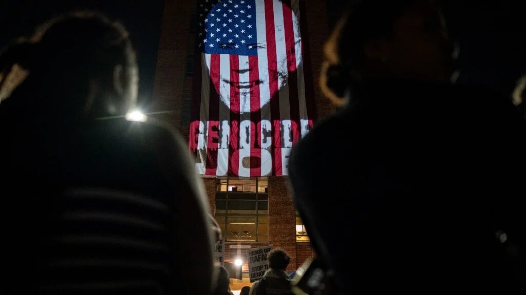 Manifestants pro-palestiniens rassemblés devant projection du visage du président Joe Biden, l’associant au génocide à Gaza, sur un drapeau américain à l'Université George Washington, le 7 mai 2024 à Washington (Kent Nishimura/Getty Images/AFP)