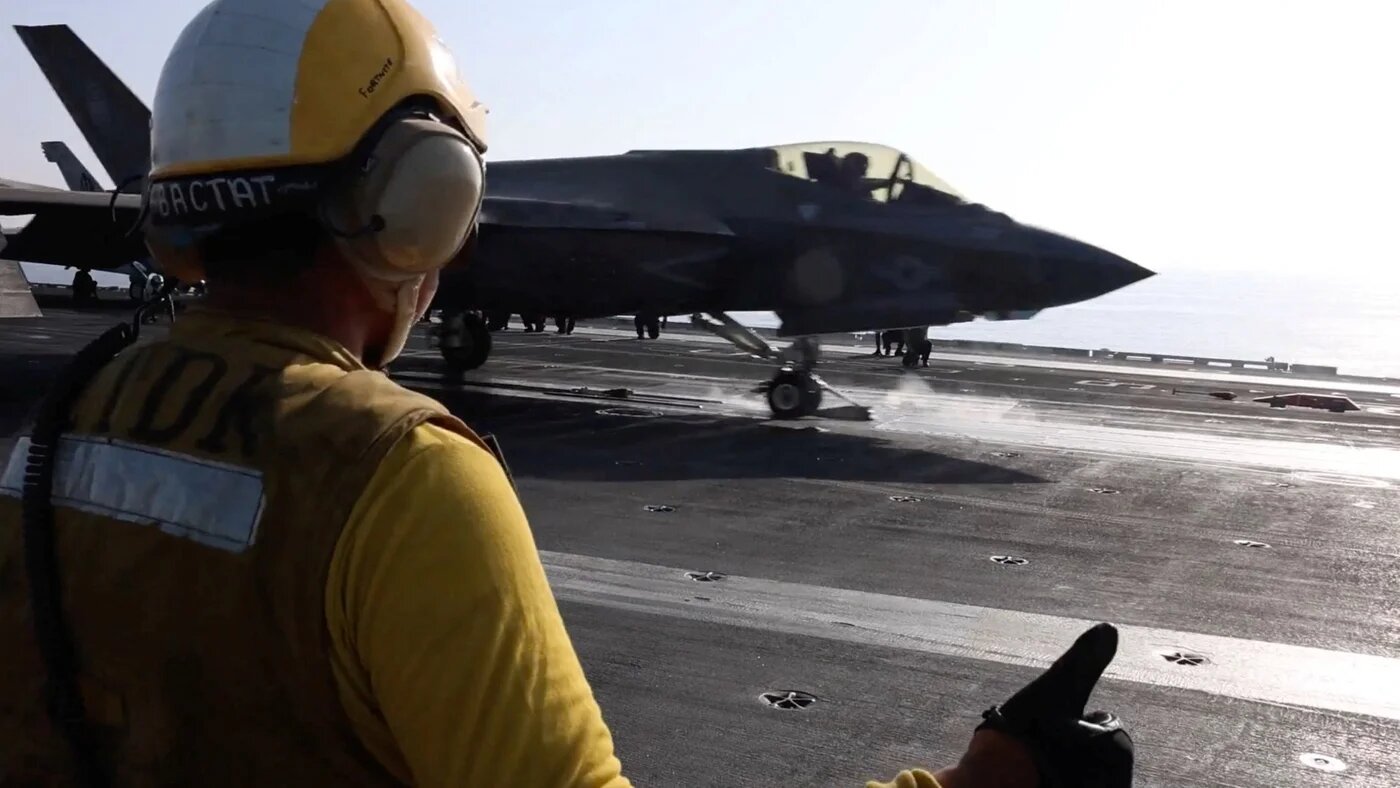 A flight deck crew member signalling an F‑35 jet on a US aircraft carrier (Centcom via Reuters)