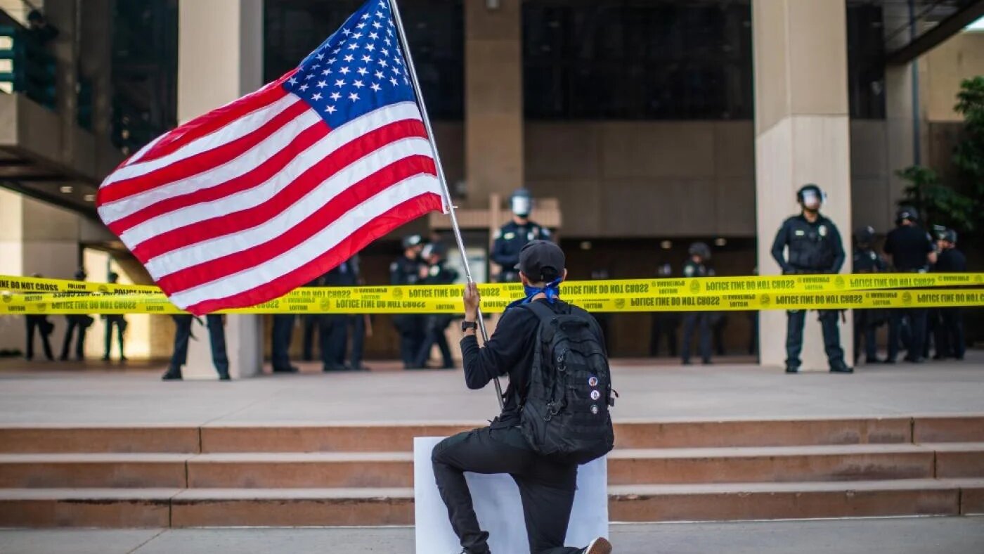 À Anaheim, en Californie, un manifestant tenant un drapeau américain s’agenouille devant des policiers au cours d’une manifestation pacifique suite à la mort de George Floyd, le 1er juin (AFP)