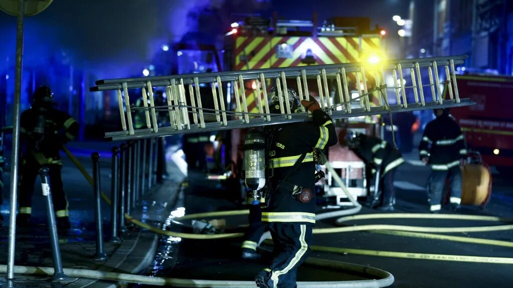 Des pompiers marchent avec du matériel après avoir éteint un incendie dans un hôtel lors de manifestations à Roubaix, dans le nord de la France, le 30 juin 2023 (AFP/Kenzo Tribouillard)