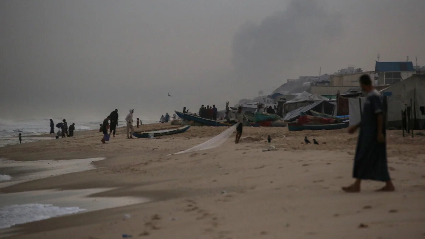 Smoke billows in the background from Israeli strikes in the northern Gaza Strip in a makeshift camp by the beach in Al-Zawayda city, near Deir al-Balah, in the central Gaza Strip on 9 October 2025 (AFP/Bashar Taleb)