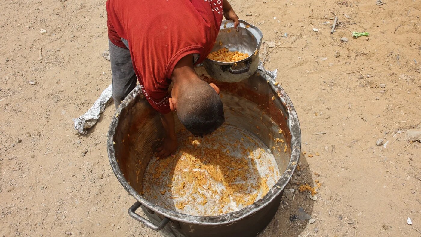A Palestinian boy scrapes out leftovers from the bottom of a pot at a charity kitchen providing hot meals in Gaza City on 12 May 2025 (Omar al-Qattaa/AFP)