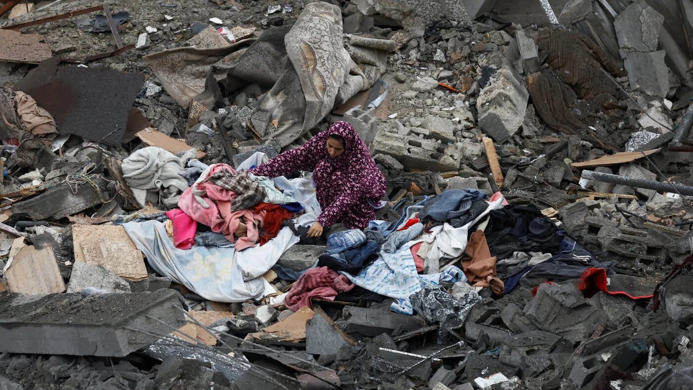 A Palestinian woman gathers her belongings at the site of Israeli strike on a house, in the central Gaza Strip, 9 January 2026 (Mahmoud Issa/Reuters)