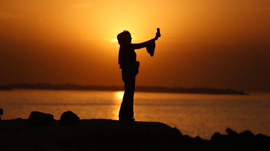 A woman holds a mobile phone during a film screening and entertainment event in Gaza’s al-Shati refugee camp, on 23 November 2025 (Omar al-Qattaa/AFP)