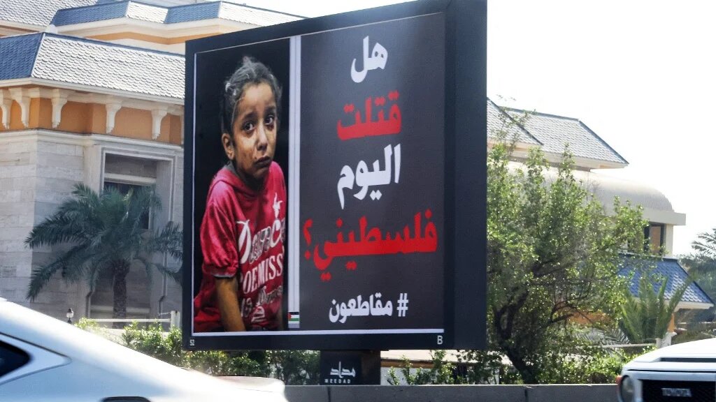 Des voitures passent devant un panneau publicitaire avec la photo d’un enfant palestinien et une inscription en arabe indiquant « Avez-vous tué un Palestinien aujourd’hui ? #boycott » à Koweït City le 26 octobre 2023 (AFP/Yasser al-Zayyat)