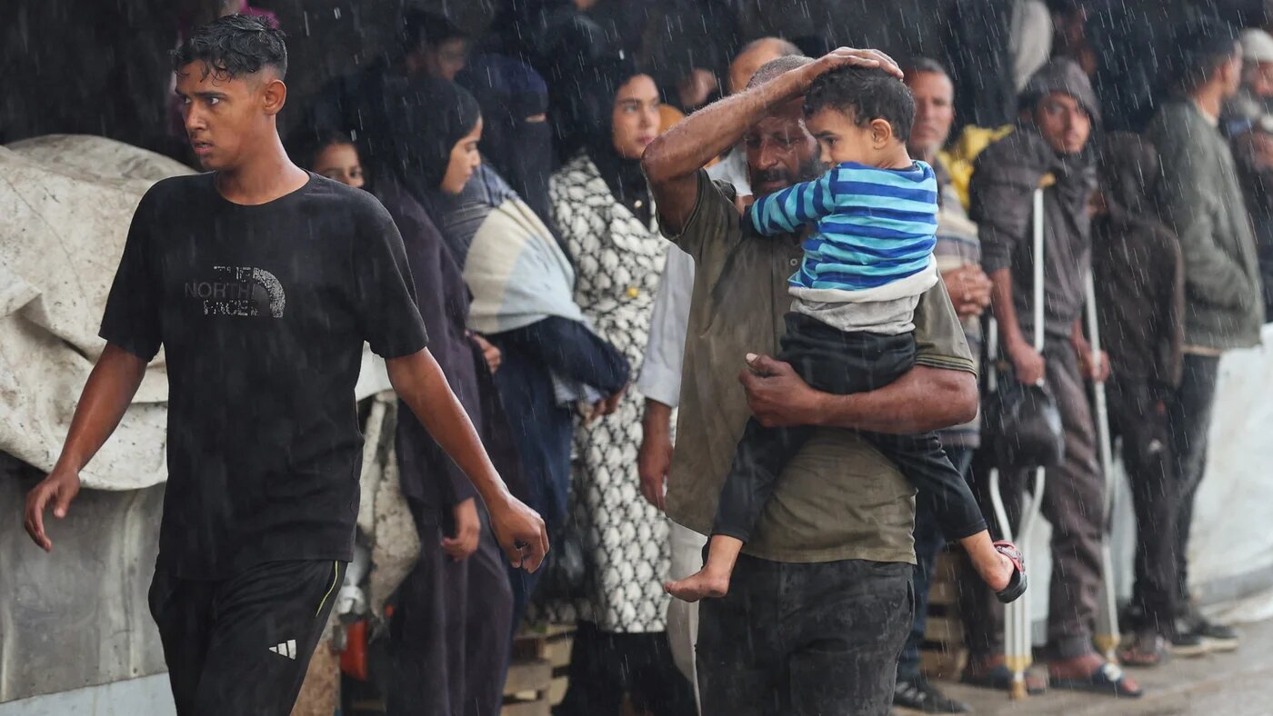 A Palestinian shields a child from the rain as they rush to shelter during a downpour in Khan Younis, in the southern Gaza Strip, 25 November 2025 (Reuters)