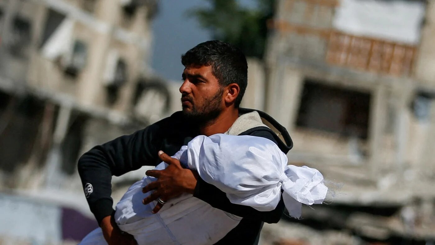 A Palestinian man carries the body of a child killed in Israeli strikes in Jabalia, northern Gaza, on 16 May 2025 (Reuters/Mahmoud Issa)