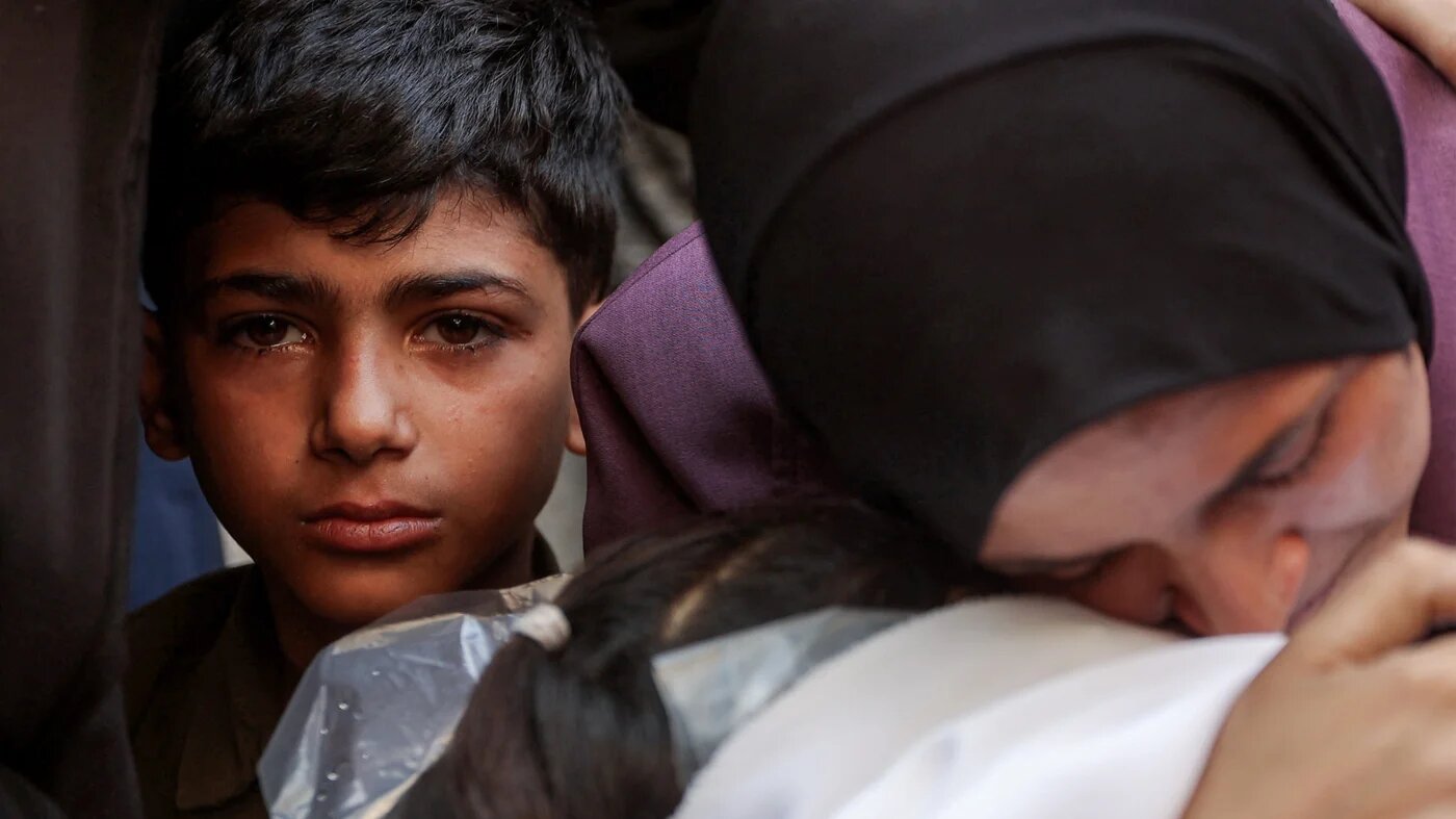 A boy looks on as a woman mourns over the body of a victim killed during overnight Israeli bombardment as she sits at al-Shifa hospital in Gaza City on 4 June 2025 (Omar al-Qattaa/AFP)
