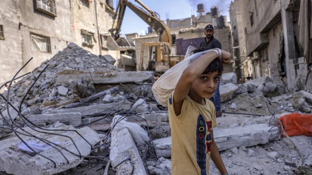 A Palestinian boy looks on as workers clear the rubble of a building destroyed by Israeli bombing during the 2021 war, in Rafah, Gaza, on 30 September 2021 (AFP)