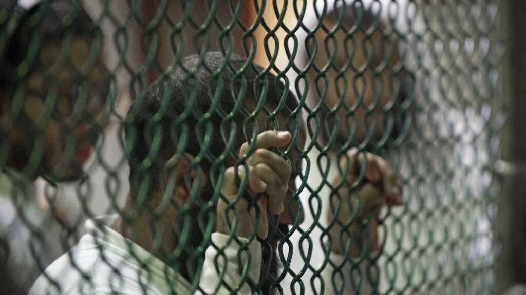 Detainees line up at a chain link fence for library books and magazines inside Camp VI at Guantanamo Bay prison in 2010