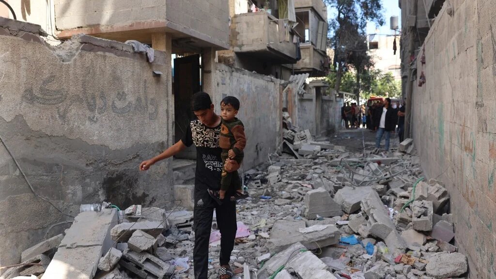 Un jeune Palestinien porte un enfant alors qu’il marche à travers des décombres, à la suite du bombardement israélien du quartier de Tal al-Sultan à Rafah, dans le sud de la bande de Gaza, le 7 mai 2024 (AFP)