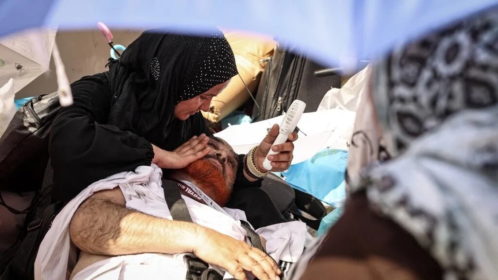 A woman uses a hand-held fan to cool a man affected by the scorching heat during the symbolic 'stoning of the devil' ritual at the annual Hajj pilgrimage in Mina on 16 June 2024 (AFP)
