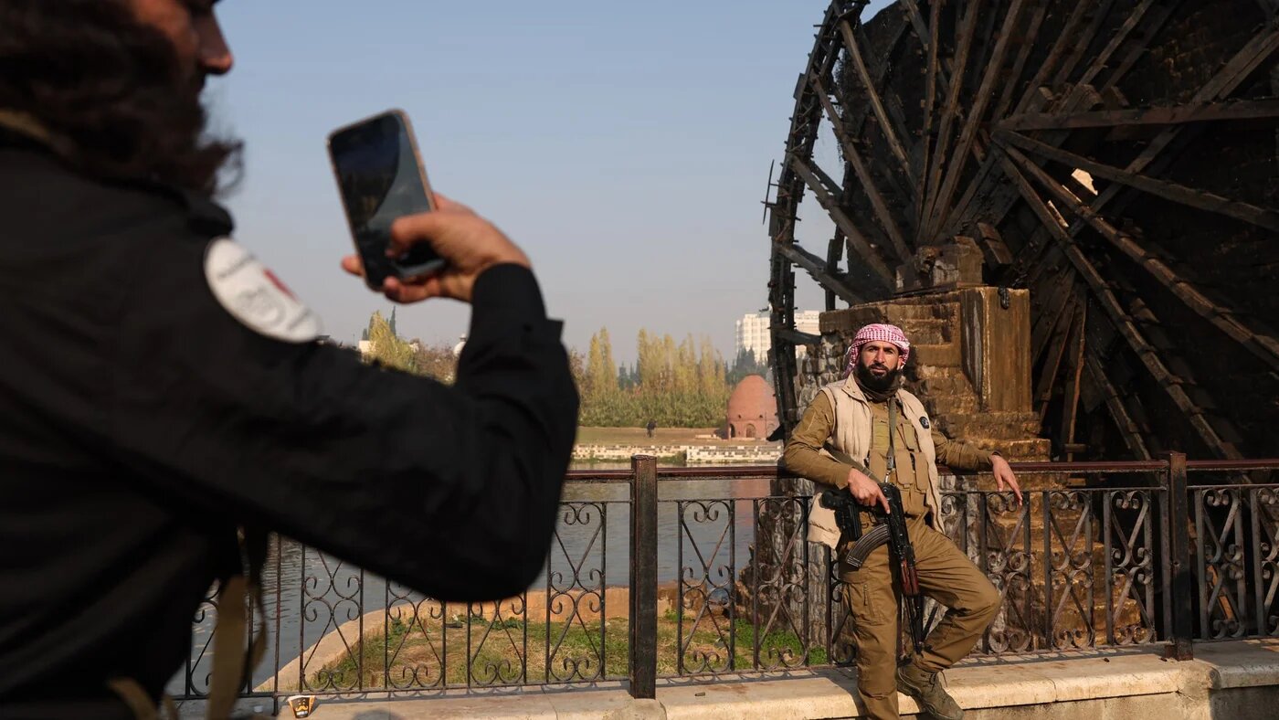 A Syrian rebel poses for a picture in front of one of the water wheels of Hama after forces captured the city on 6 December 2024 (Omar Haj Kadour/AFP)