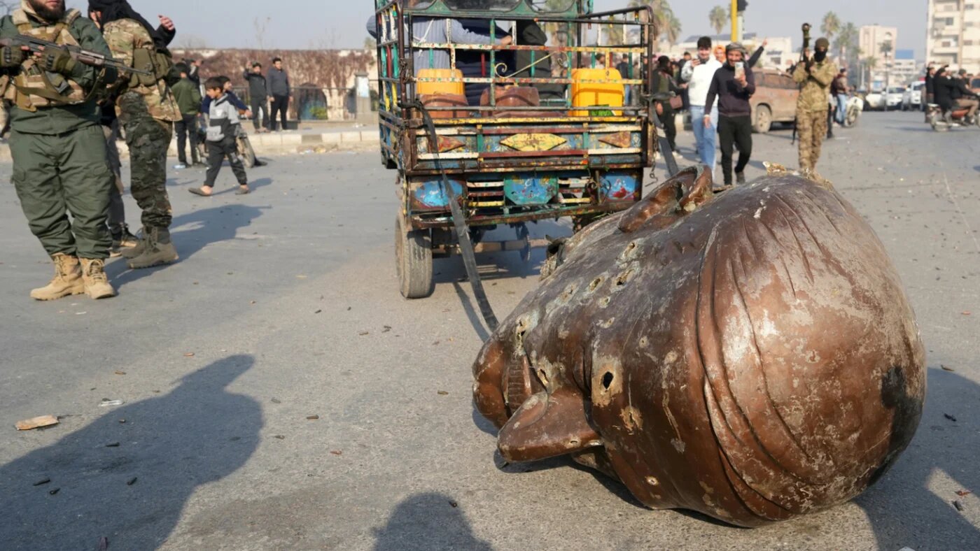 A truck pulls the head of the toppled statue of late Syrian president Hafez al-Assad through the streets of the captured central-west city of Hama on 6 December 2024 (Muhammad Haj Kadour/AFP)