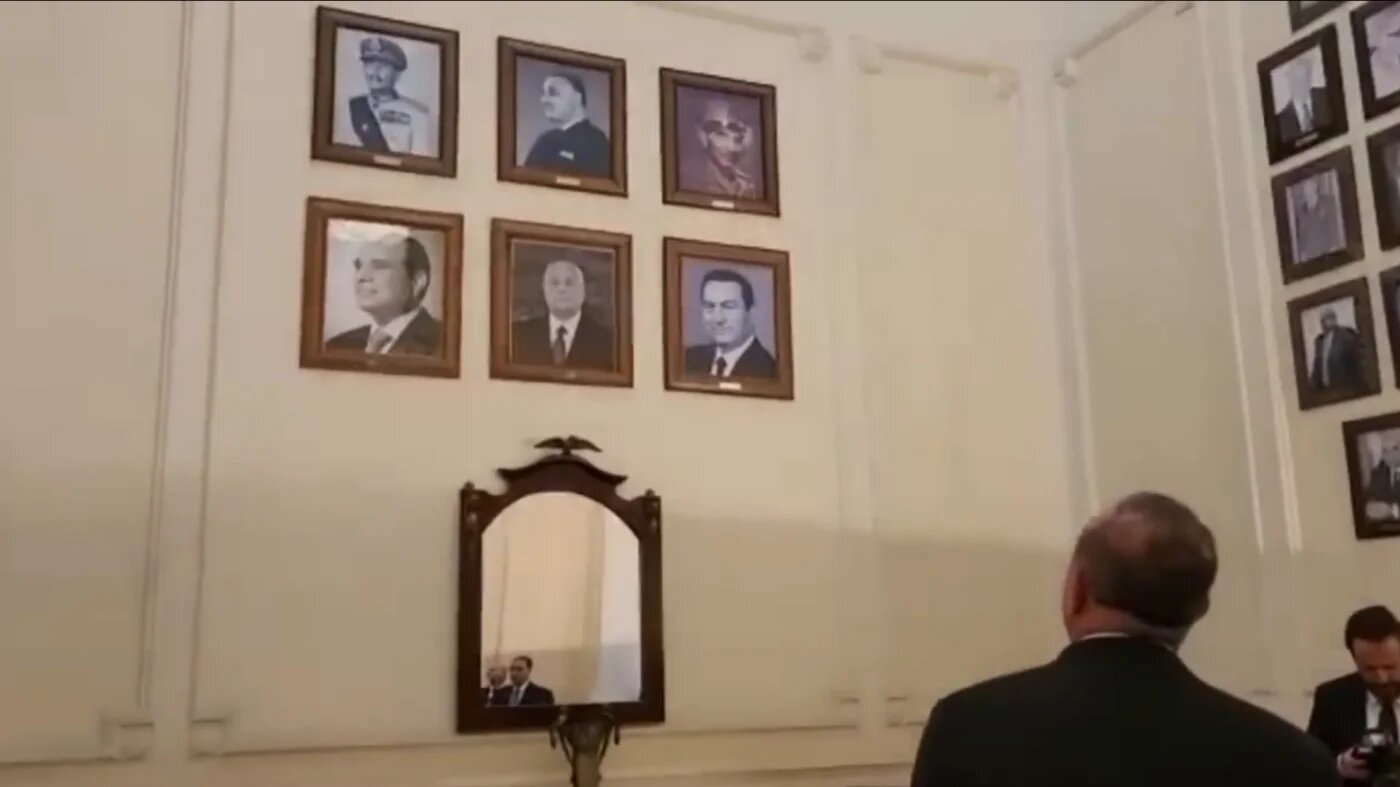 Turkey's Foreign Minister Mevlut Cavusoglu standing in front of a wall of pictures that features Egypt's presidents in Cairo (Screengrab)