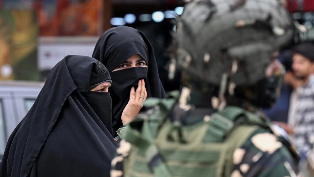 Kashmiri Muslim women walk along a street as an Indian paramilitary trooper stands guard in Srinagar on 2 May 2025 (Tauseef Mustafa/AFP)