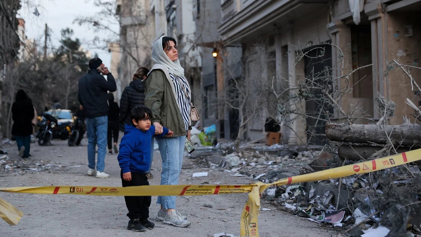 A woman with her child looks at the aftermath of an Israeli and US strike on a police station in Tehran, Iran, 2 March 2026 (Majid Asgaripour/WANA via Reuters)