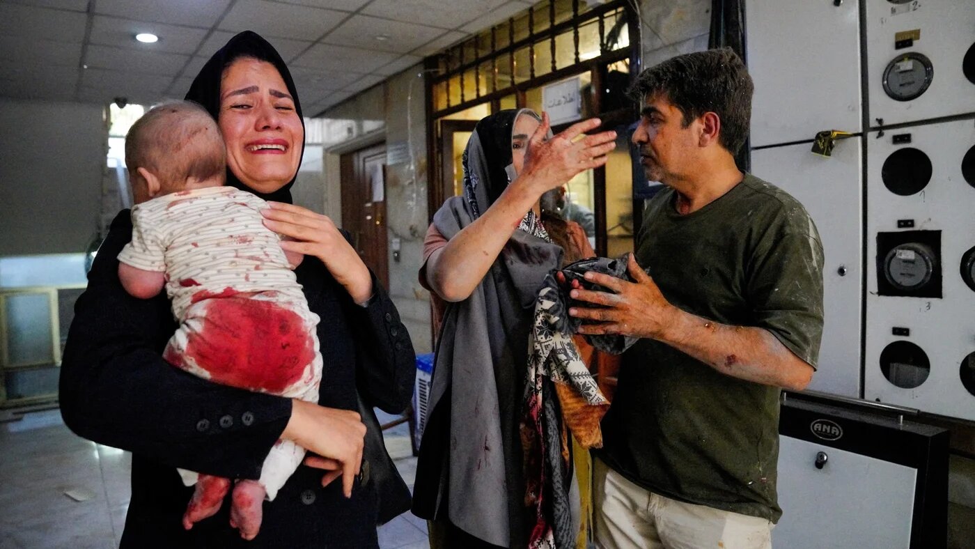 A woman carries her child following the Israeli strikes on the Iranian capital Tehran on 15 June 2025 (Amir Kholousi/West Asia News Agency via Reuters)