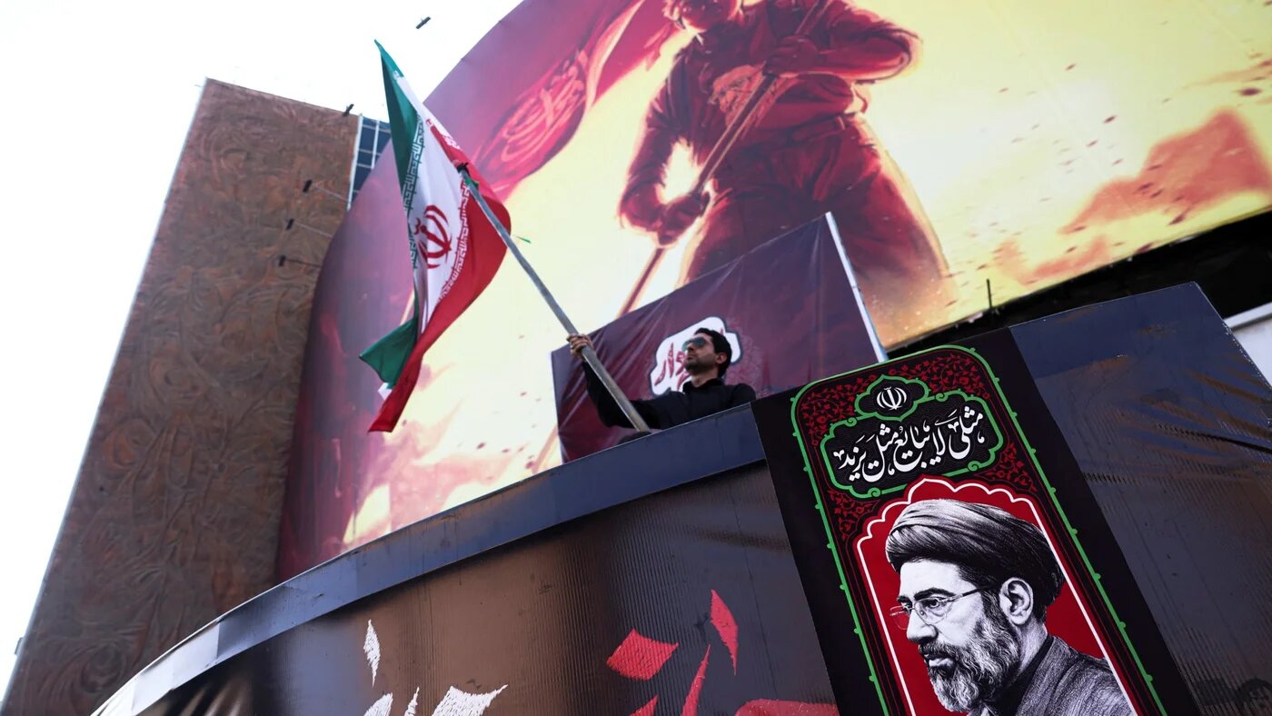 A man holds an Iranian flag, next to a picture of Iran's Supreme Leader Mojtaba Khamenei, in Tehran, Iran, on 13 August 2026 (Majid Asgaripour/West Asia News Agency via Reuters)