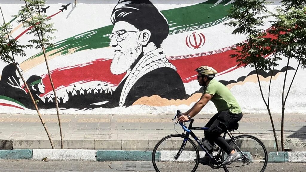 A man cycles past a mural depicting the late Iranian supreme leader, Ayatollah Ali Khamenei, in Tehran on 24 July 2026 (AFP)
