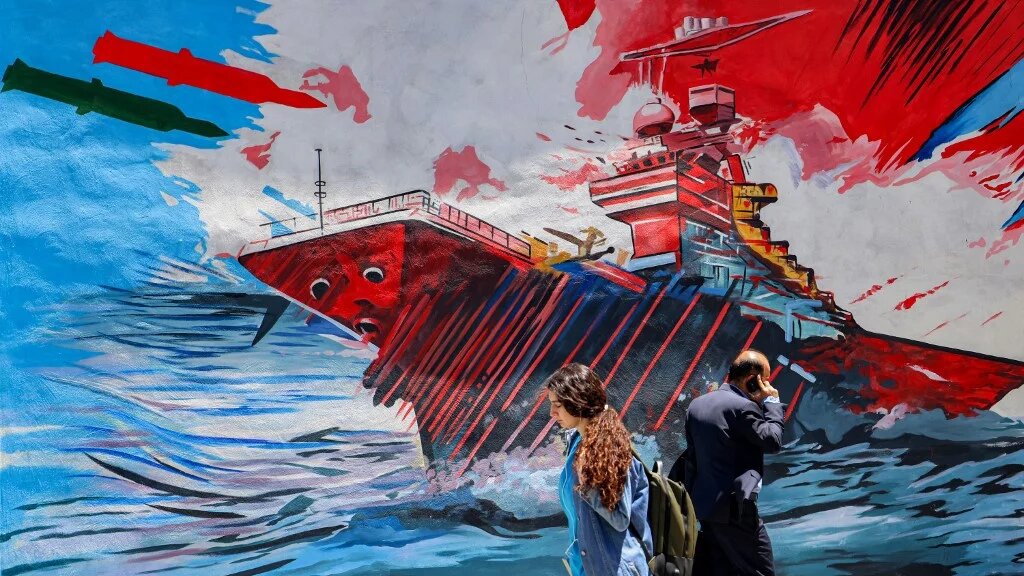 People walk past a mural that depicts missiles hitting an aircraft carrier, amid the US-Israeli war on Iran, in Tehran on 26 May 2026 (Atta Kenare/AFP)