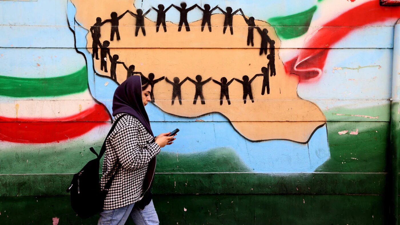 A woman walks past the flag and map of Iran painted on a wall in Tehran on 25 February 2026 (AFP)