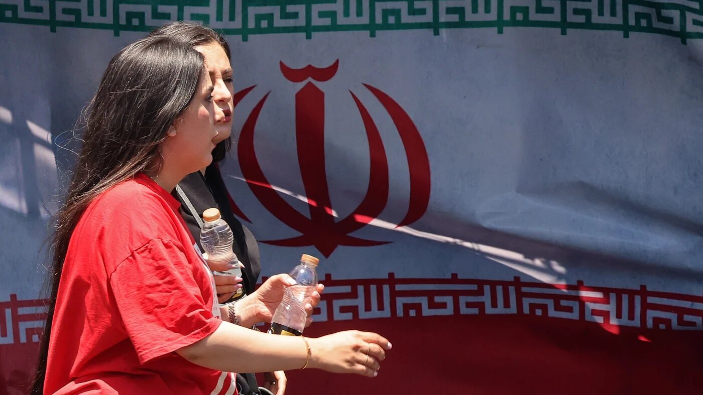 Iranian women walk past Iran's national flag at Vanak Square in Tehran on 10 June 2026 (Atta Kenare/AFP)