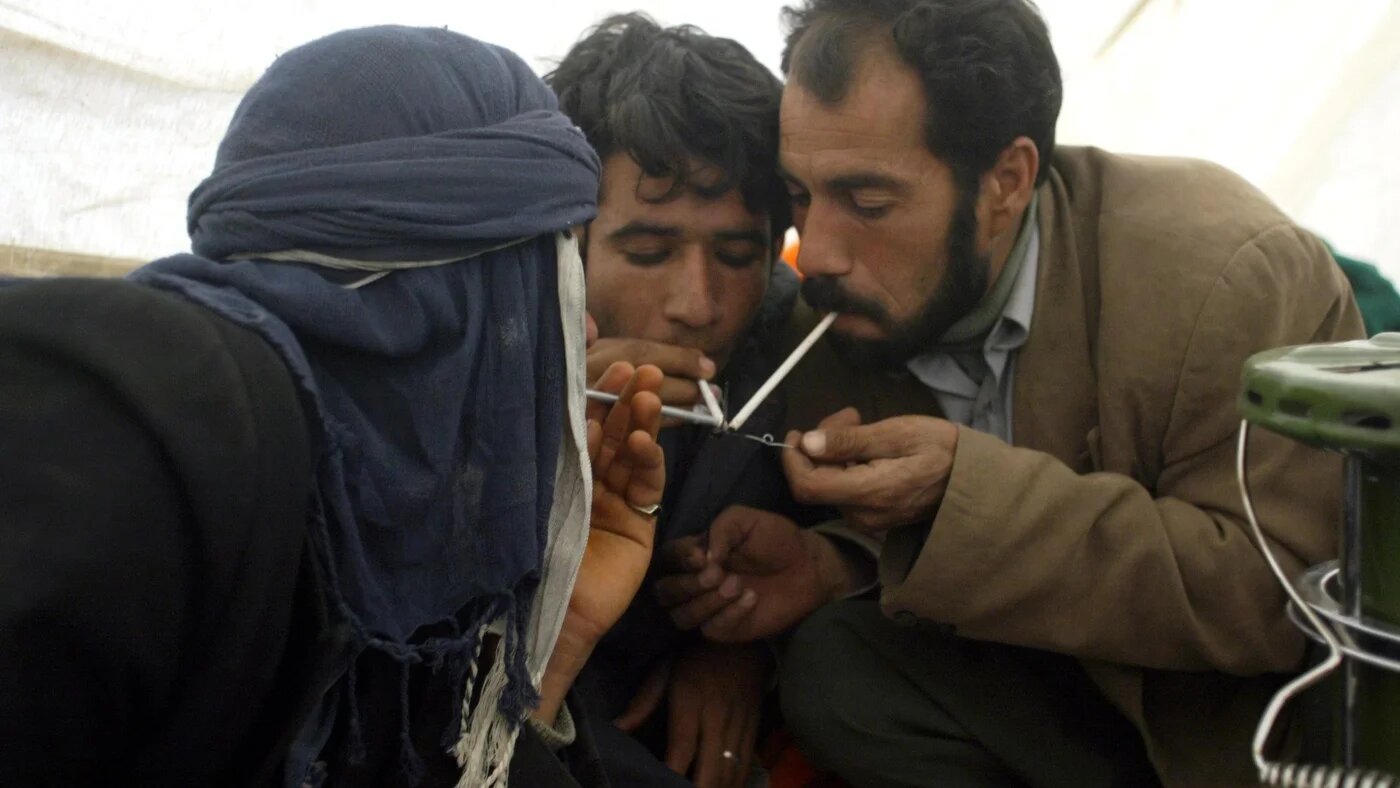 Iranian men smoke opium in a tent in the southeastern Iranian city of Bam on 31 December 2003 (AFP)