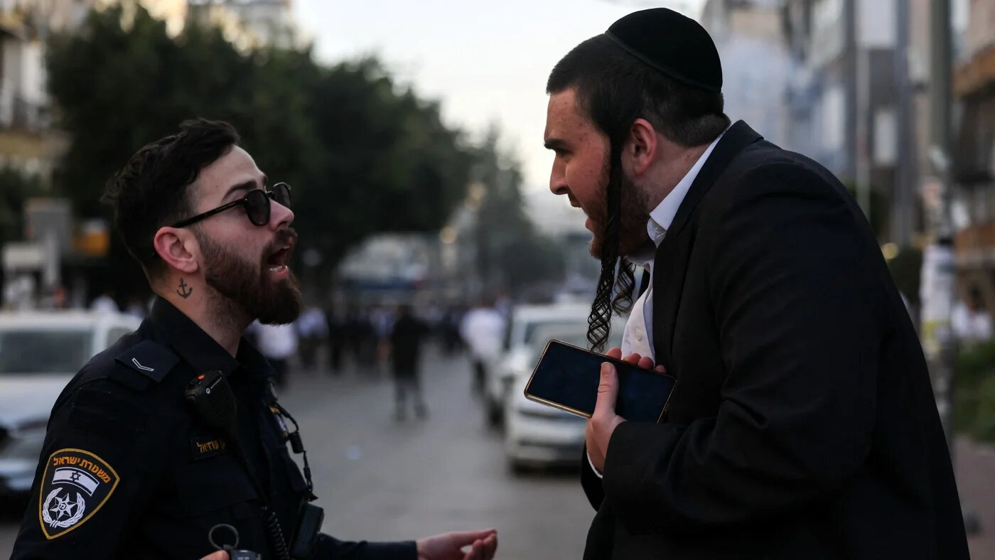 A member of the Israeli police speaks to a man during a protest against pressure to conscript the ultra-Orthodox Jewish community into Israel's military, in Bnei Brak, Israel, 15 February 2026 (Reuters/Nir Elias)