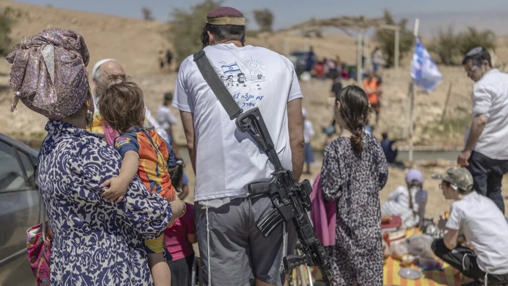 An armed Israeli settler is seen in the occupied West Bank village of Ras Ein al-Auja, whose Bedouin community was displaced earlier this year, on 22 April 2026 (Ilia Yefimovich/AFP)