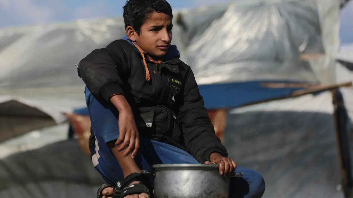 A displaced Palestinian boy waits with his container to receive food at a charity kitchen in Khan Younis, south Gaza, on 17 December, 2025 (AFP/Bashar Taleb)