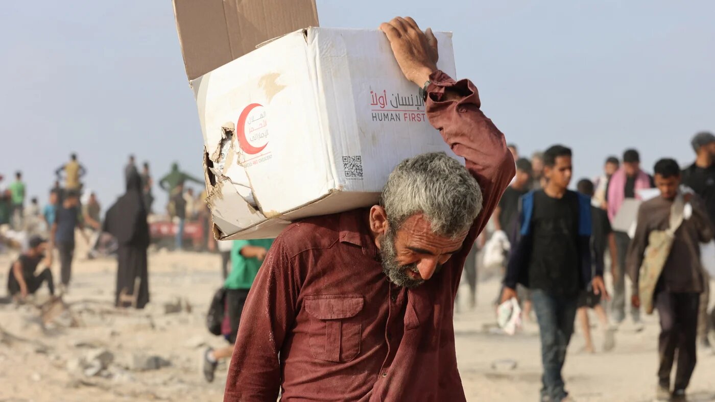 A Palestinian man carries a box of aid along al-Rashid street in western Jabalia on 22 June, 2025 (AFP/Omar al-Qattaa)