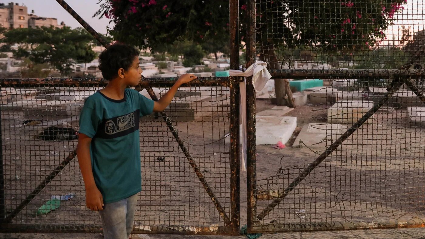 A Palestinian child looks through a fence at Falluja cemetery where five children, among them four cousins, were killed by an Israeli strike on 7 August 2022 in Gaza (MEE/Mohammed al-Hajjar)