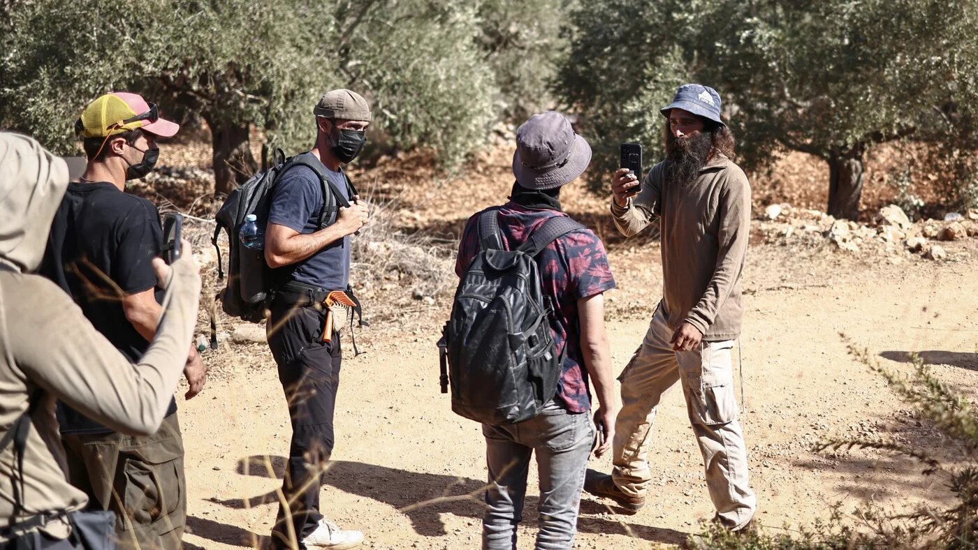 An Israeli settler (R) uses his mobile phone as he records foreign volunteers (L) in an olive grove, after disrupting Palestinian farmers' olive harvest near the occupied West Bank village of Turmus Ayya on 28 October 2025 (AFP/Zain Jaafar)