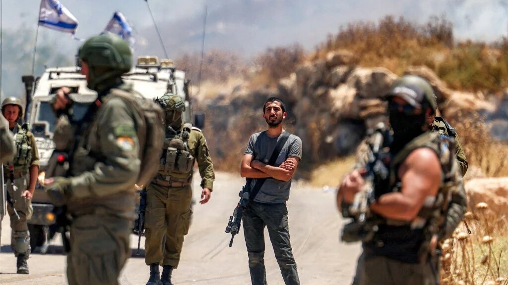 An Israeli settler stands among Israeli forces gathering near Palestinian protesters in the village of Idna, in the occupied West Bank, on 5 June 2026 (Hazem Bader/AFP)