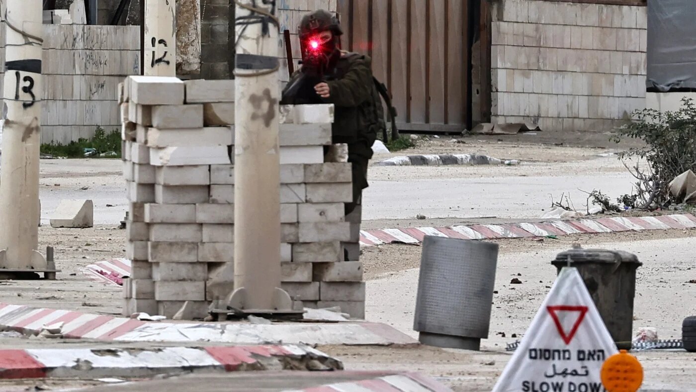 An Israeli soldier takes aim while manning a checkpoint during a raid in the Nour Shams refugee camp near Tulkarm in the occupied West Bank on 9 February 2025 (AFP/Zain Jaafar)