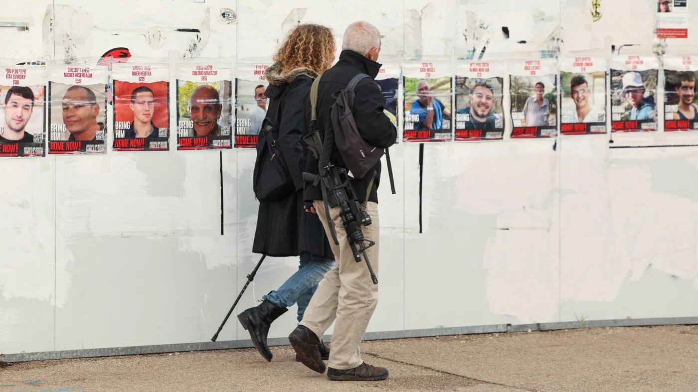 A man carrying a rifle walks with a woman outside the Israeli Parliament in Jerusalem on 15 January 2024 (Ahmad Gharabli/AFP)