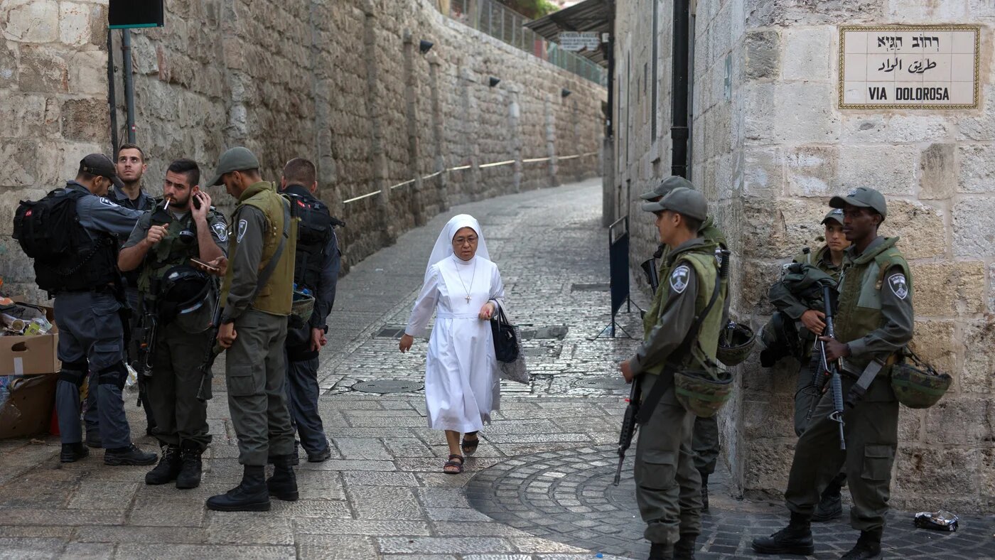 A nun walks past Israeli police as they stand on the historic Via Dolorosa street in the Old City of Jerusalem (Menahem Kahana/AFP)