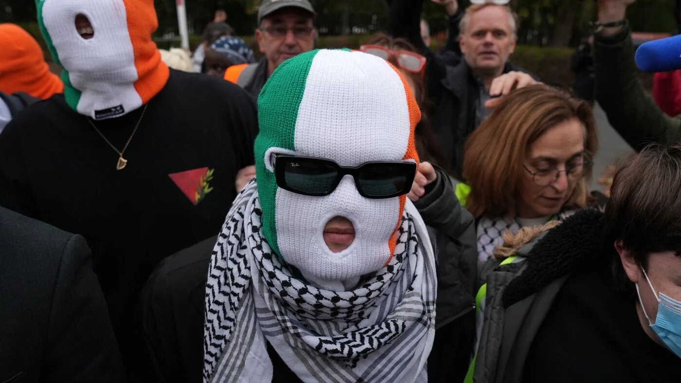 Members of the band Kneecap, including singer Liam O'Hanna who performs under the stage name Mo Chara, wear Irish flag-themed balaclavas as they arrive at Woolwich Crown Court in south east London on 26 September 2025 (AFP/Carlos Jasso)