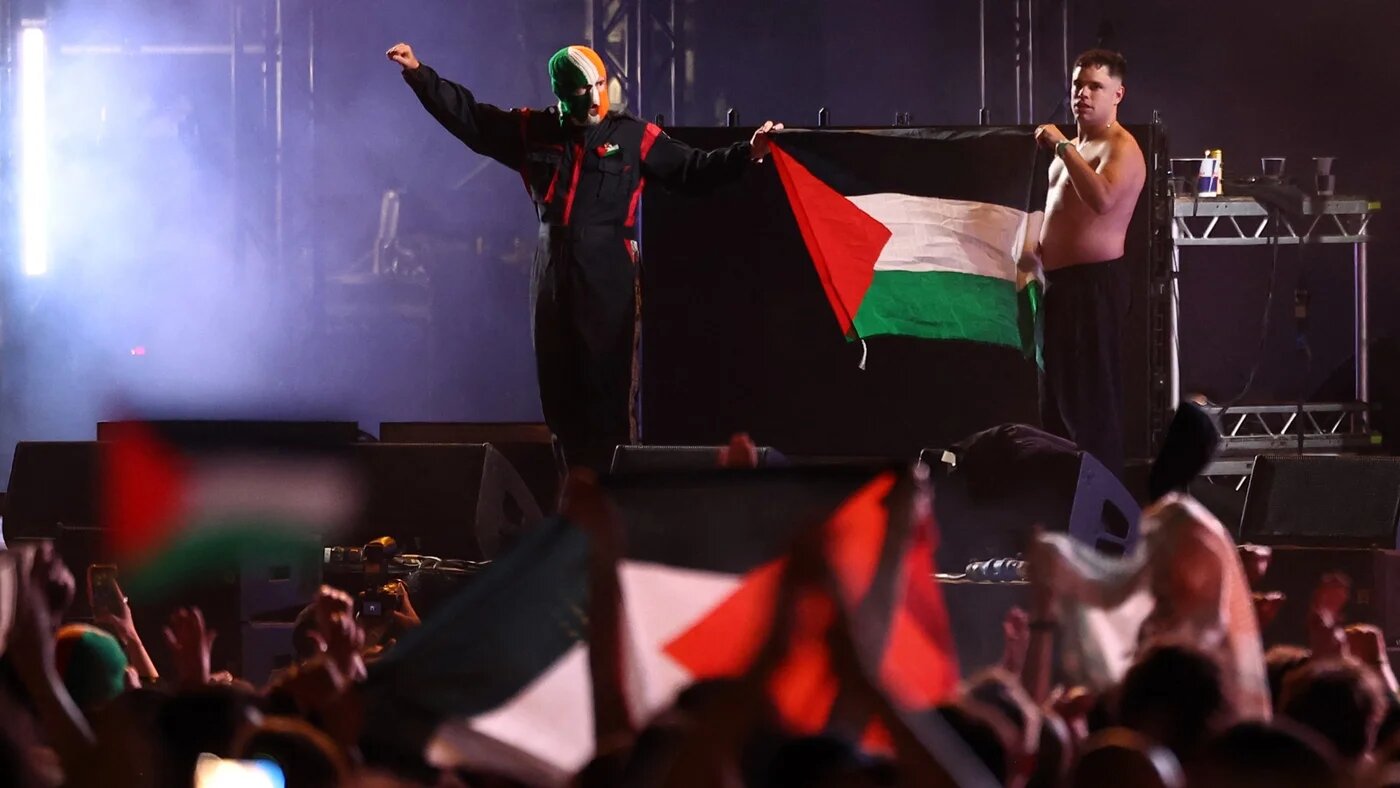 Naoise O Caireallain (R) and JJ O'Dochartaigh of band Kneecap hold up a Palestine flag after performing onstage during Wide Awake Festival 2025 at Brockwell Park in south London on 23 May 2025 (AFP/Henry Nicholls)