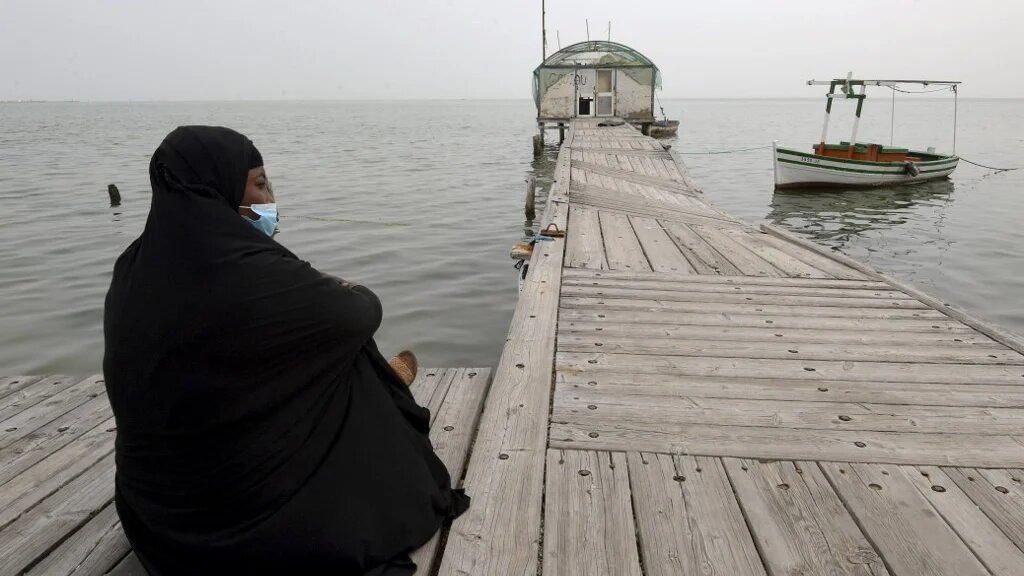 Une migrante d’Afrique subsaharienne, assise sur un ponton de Sidi Mansour, à 270 km au sud-est de Tunis, attend une opportunité pour partir en Europe (AFP/Fethi Belaïd)