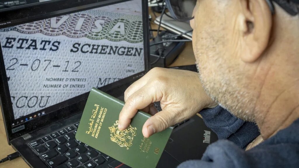 A Moroccan man holds his passport in front of his computer displaying a Schengen visa in the capital Rabat, on 28 September, 2021 (AFP)