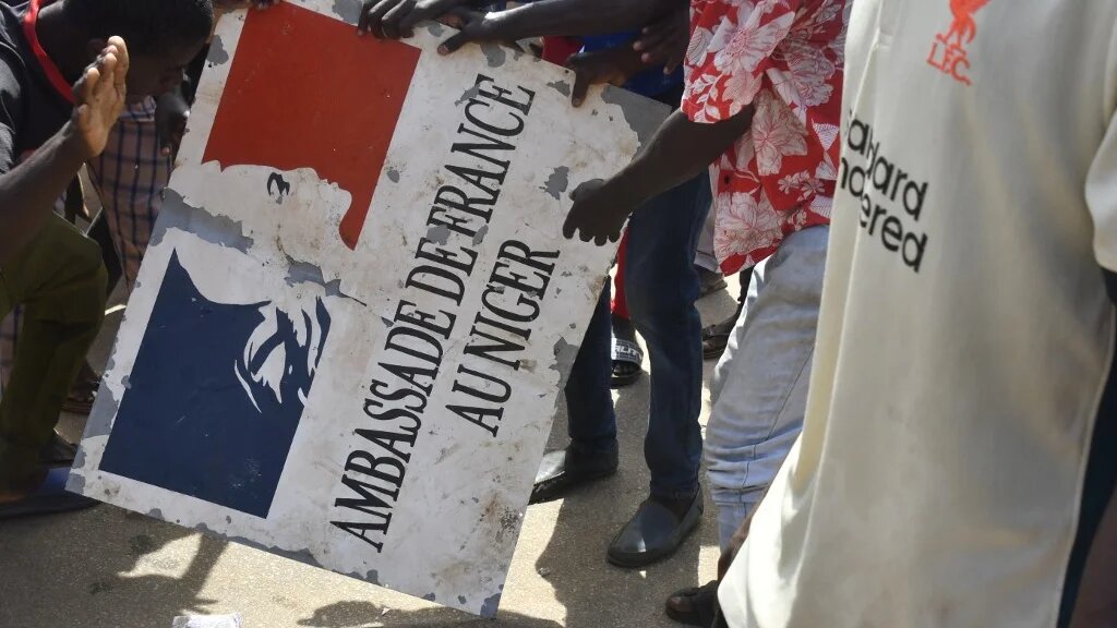 Des manifestants tiennent une pancarte décrochée de l’ambassade de France à Niamey, lors d’une manifestation qui a suivi un rassemblement de soutien aux militaires putschistes, à Niamey, le 30 juillet 2023 (AFP)