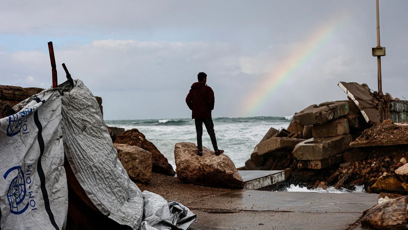 A displaced Palestinian man stands outside the family tent shelter erected in the harbour as the region experiences rain and cold winter conditions, in Gaza City on 28 December 2025 (Omar al-Qattaa/AFP)