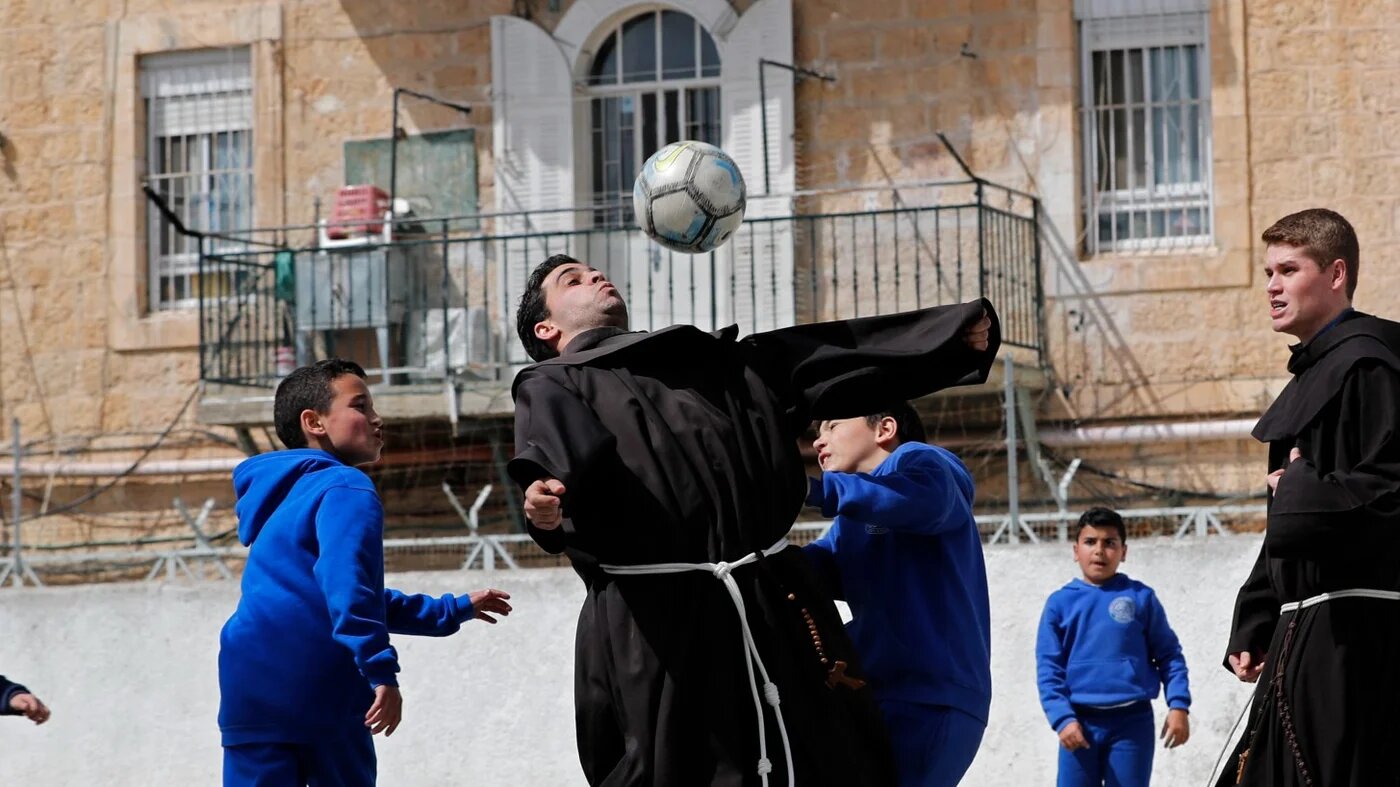 Franciscan friars play football with Palestinian children from the Terra Sancta school during a sport session in the Old City of Jerusalem, on March 1, 2018. Dispatched to the city 800 years ago by the Catholic order's founder, Saint Francis of Assisi, the Franciscans have for centuries ensured a permanent Christian presence in the Holy Land. Pilgrims know them primarily as the Guardians of the Holy Sepulchre, protecting the site where Jesus is believed to have been crucified and buried.  Thomas COEX / AFP