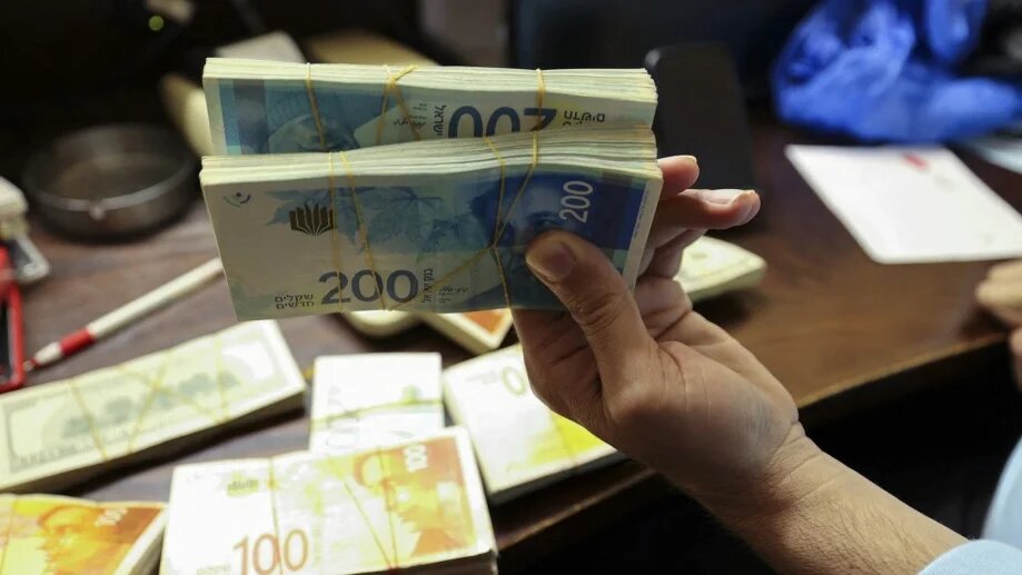 A Palestinian man counts stacks of banknotes at a currency exchange counter in the occupied West Bank city of Ramallah in October 2021 (Abbas Momani/AFP)
